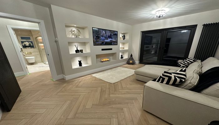 Image of a finished lounge in Basildon, Essex, with freshly painted walls, a pristine ceiling, and a painted media wall. The space features elegant glossed woodwork and a modern yet cosy atmosphere, showcasing a clean and polished design. Ideal for home renovation inspiration.